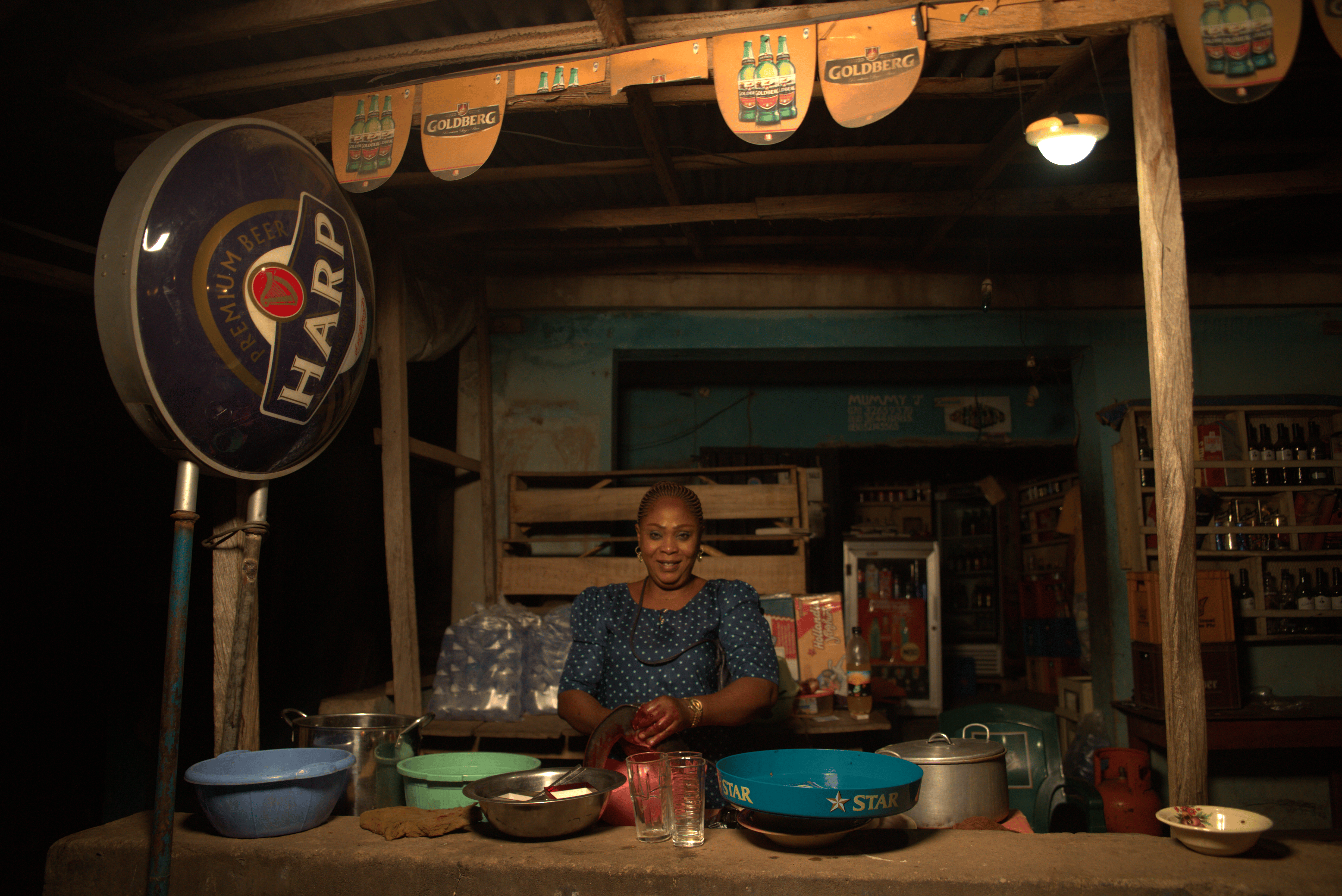 A businesswoman sits at her stall under the light of a Sun King Pro 400 solar powered lamp.