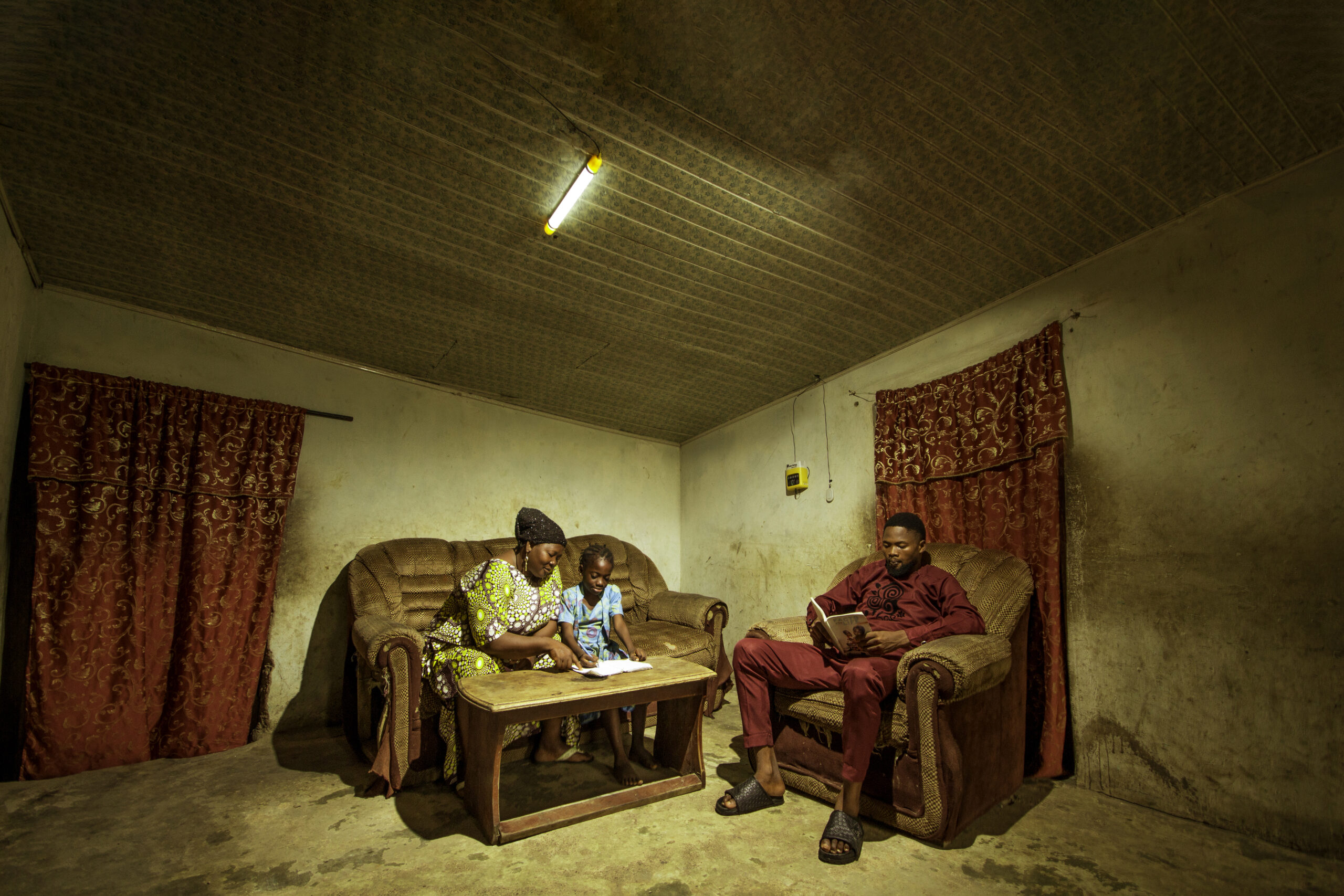 A family sits in their living room under the light of a Sun King Home 200X solar home system.