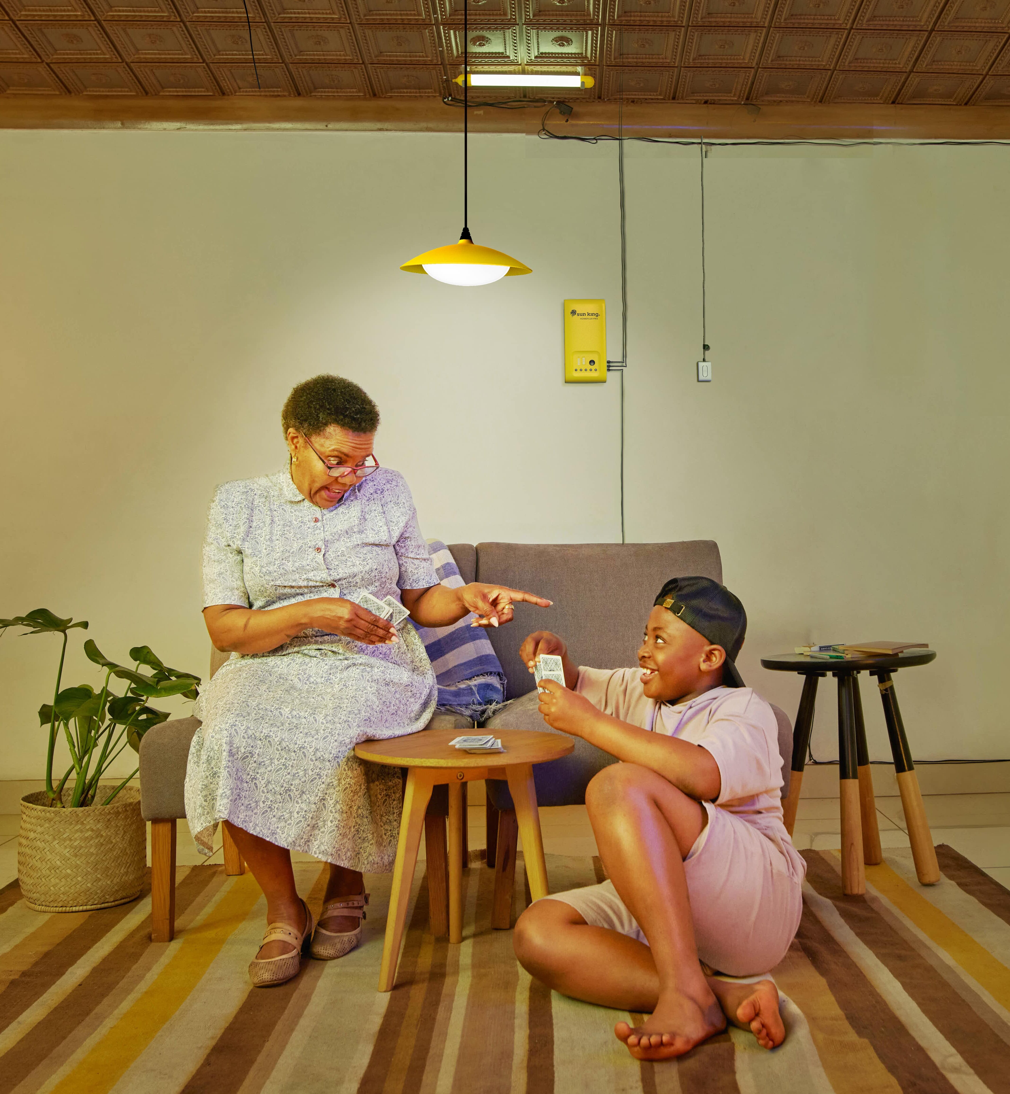 A woman and a young boy play cards under the light of their HomePlus solar home lighting and phone charging system.